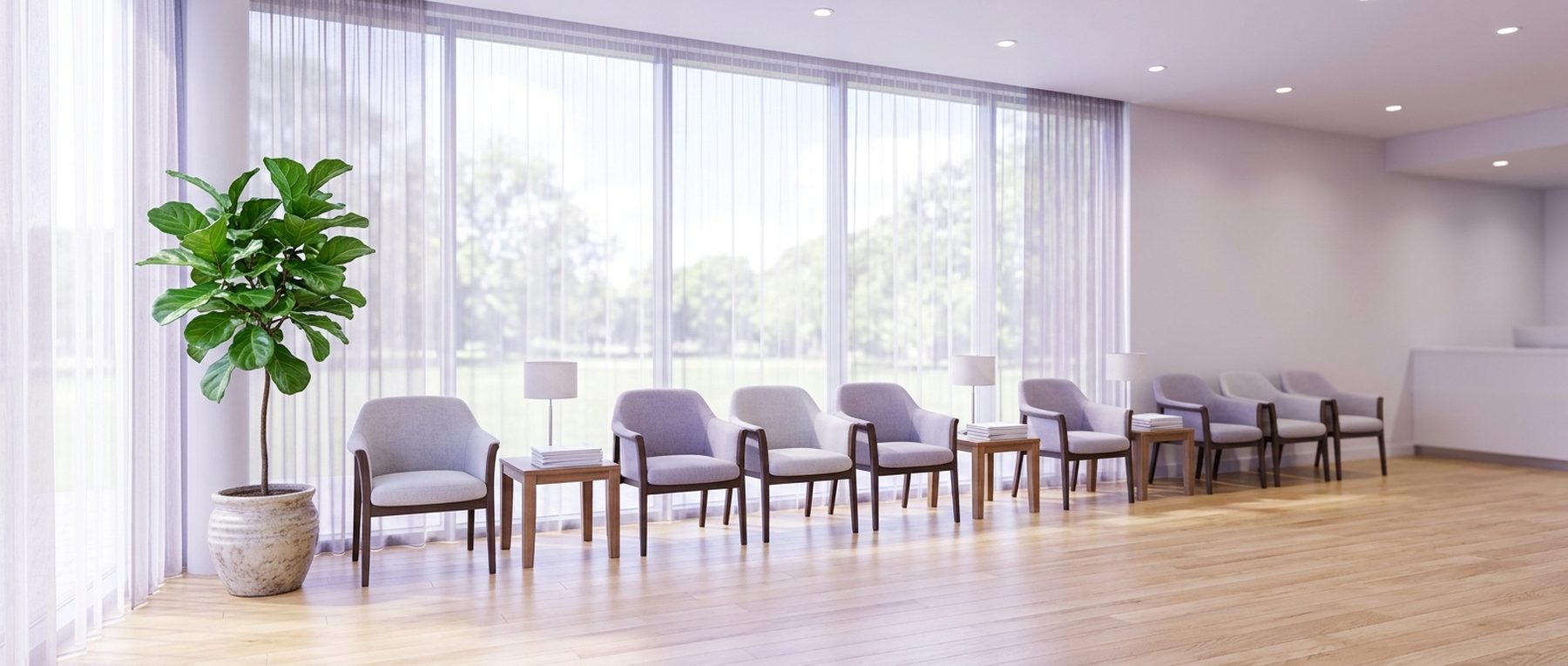 An empty, light-filled medical waiting area with upholstered chairs beside a wall of windows.